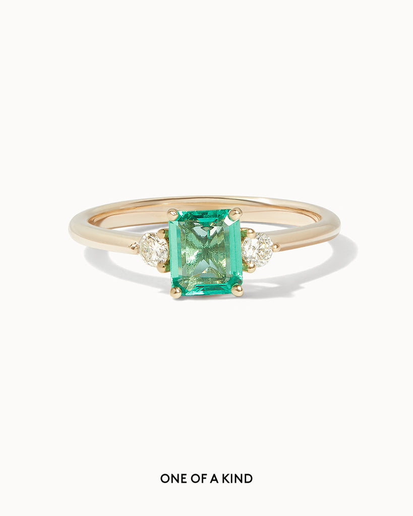 Solid gold engagement ring featuring a square emerald and two round cut white diamonds on the sides by Maya Magal London