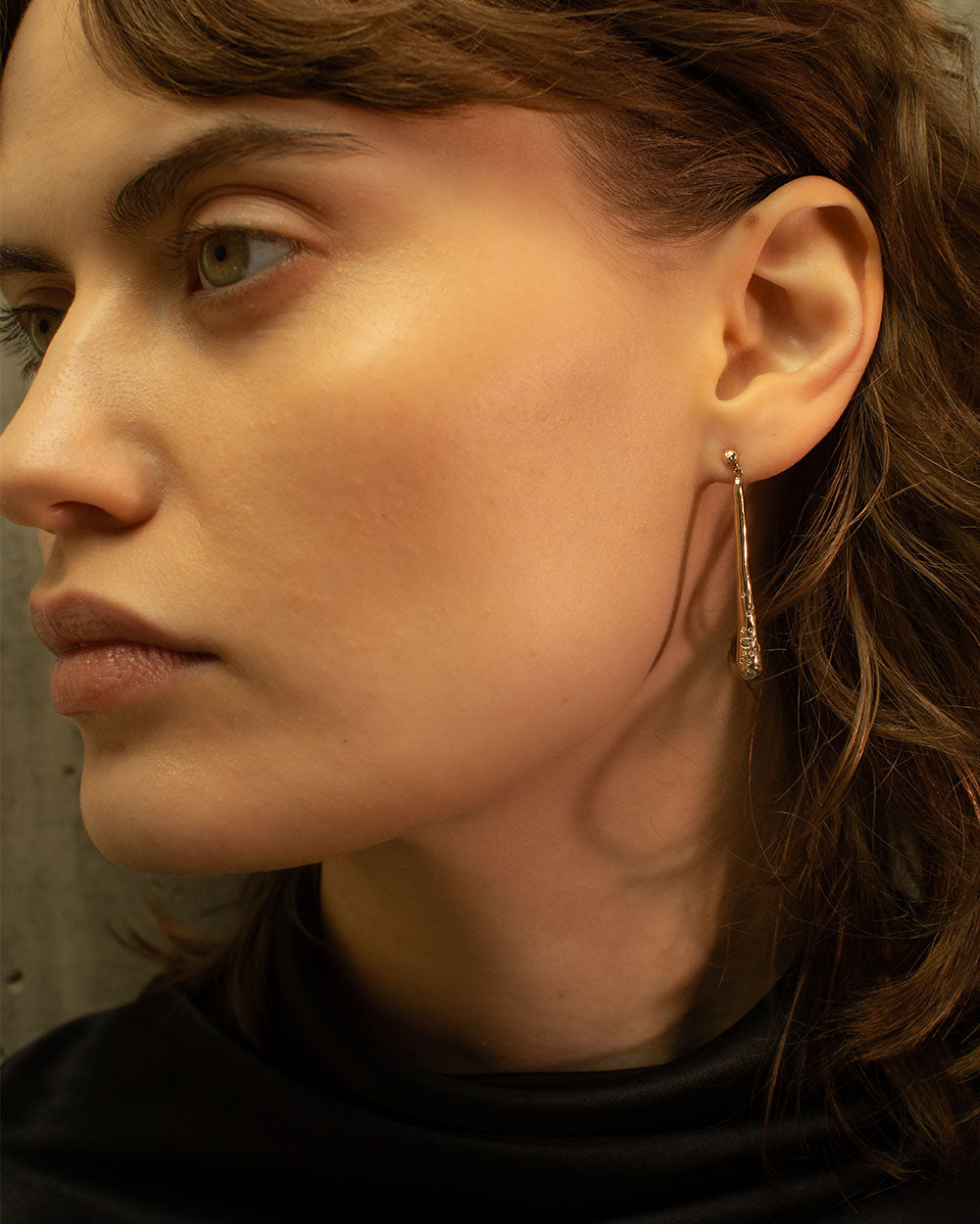 side view of model wearing 9ct solid gold drop shaped earrings set with champagne gray and white diamonds.
