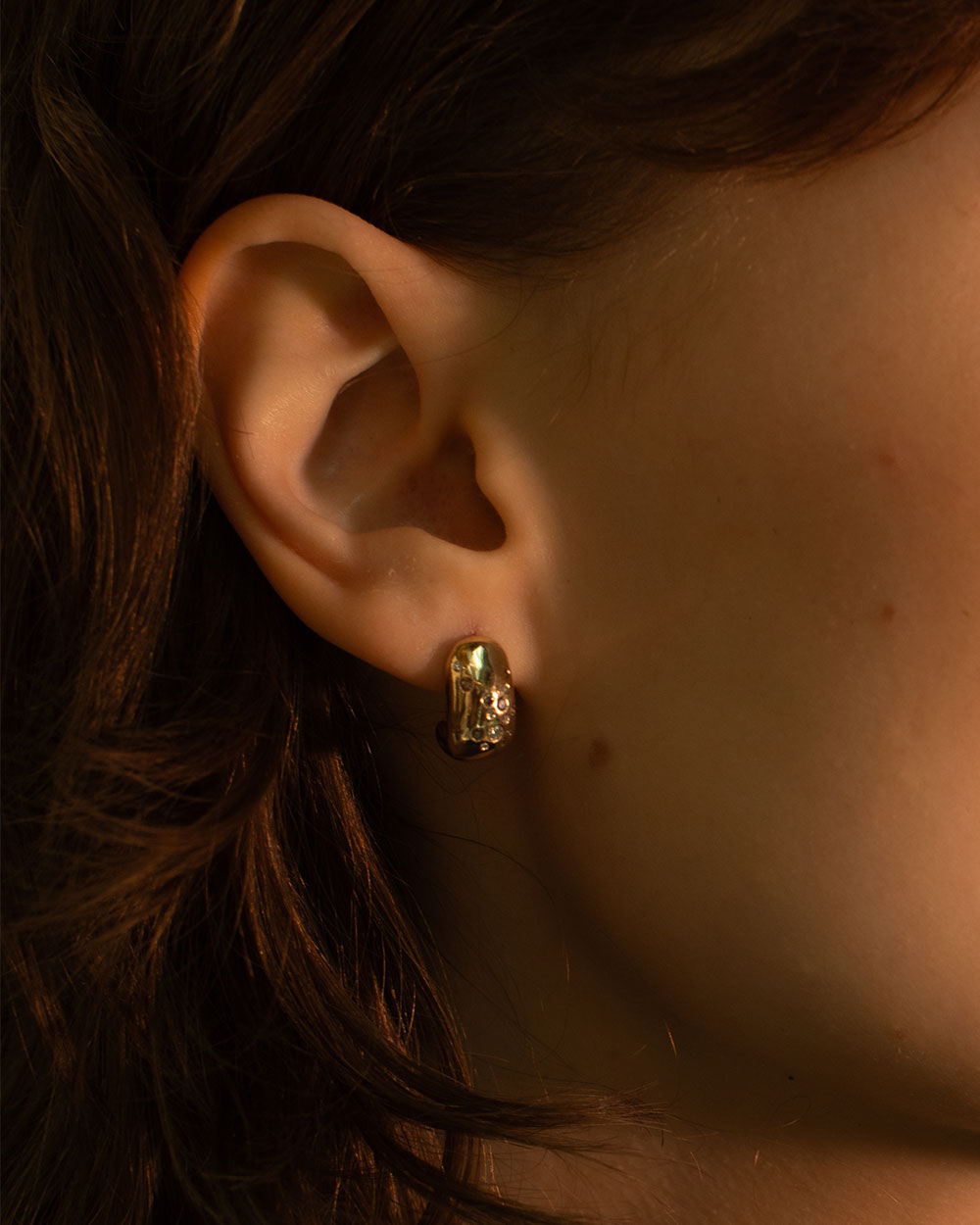 Close up of model wearing 9ct solid yellow gold hoop earrings with flush set champagne, grey and white diamonds.