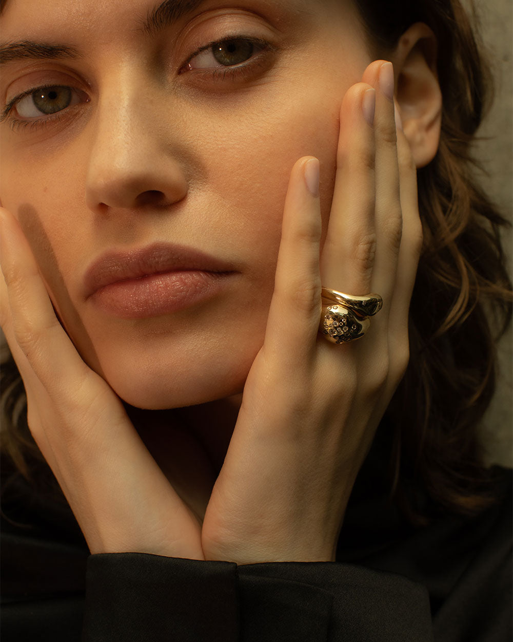 Model wearing a stack of organic 9 Ct Gold rings with flush set white and gray diamonds on a light gray background.