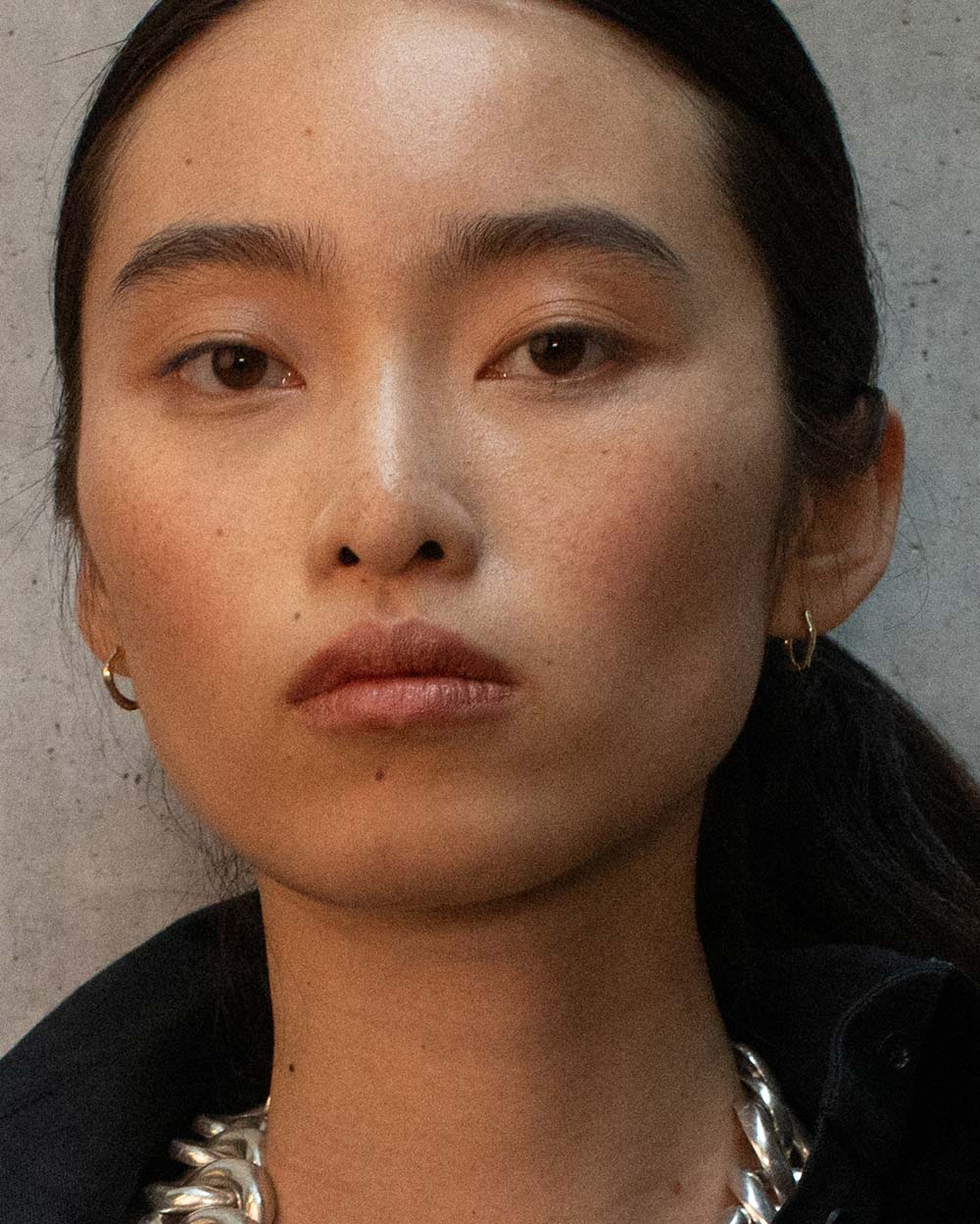 Model wearing A pair of organic textured 18ct gold plated sterling silver hoop earrings. Side view. Made with recycled materials and sustainable practices.
