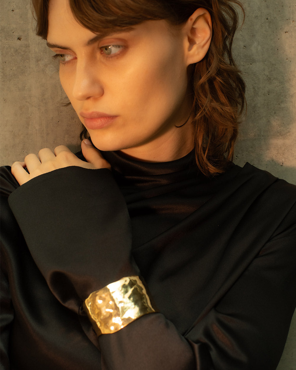Person wearing a gold arm cuff against a concrete wall.