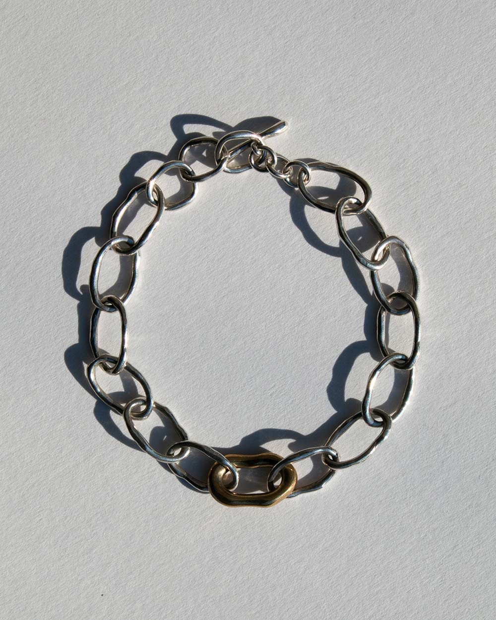 Top view of Sterling silver chain bracelet with a 9ct gold drop charm and toggle clasp, photographed on a light textured background with natural shadows.