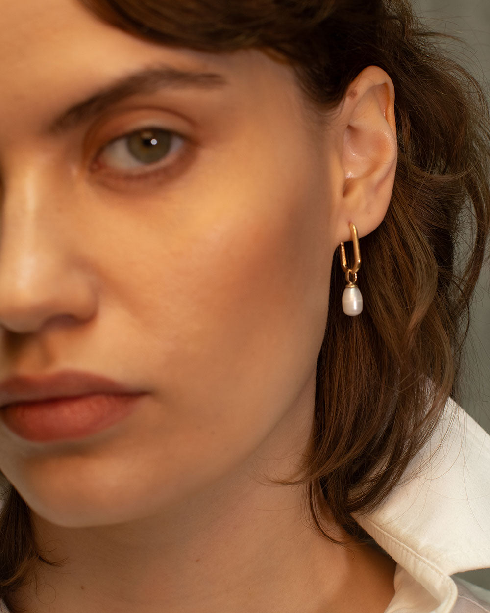 Close up of model wearing 9ct gold hoop earrings with pearl drop charms, photographed on a light textured background with natural shadows.