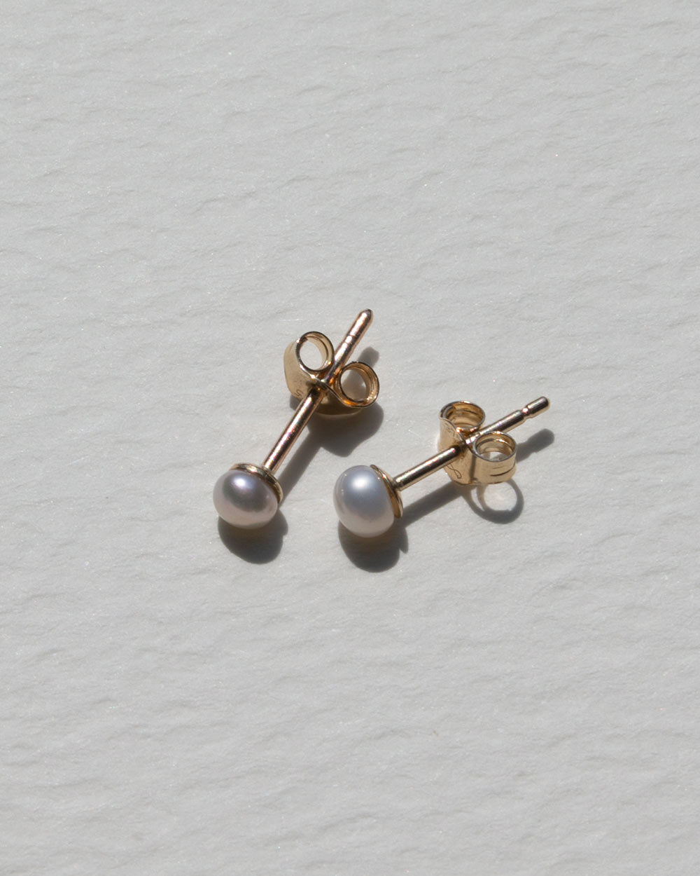 Side view of A pair of 9ct solid gold stud earrings with pearls displayed on a neutral light gray background.