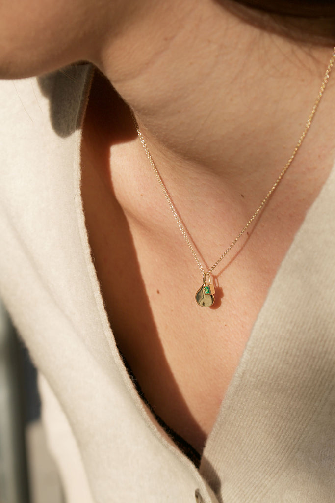 an emerald charm necklace worn around a ladies neck 