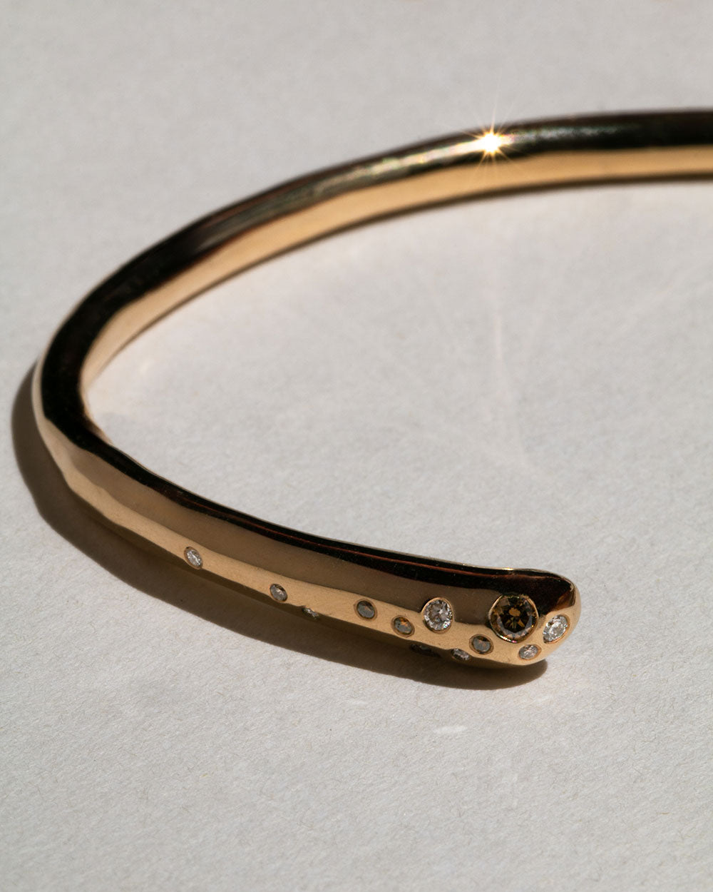 Close up of 9 ct solid gold bangle with flush set white and champagne diamonds.  An organic shape maya magal