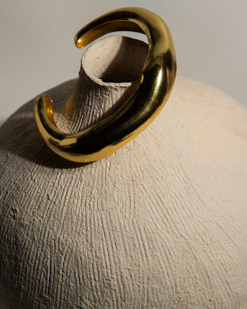 18 Ct gold plated brass MM STUDIO Lucid Bangle displayed on ceramic piece 