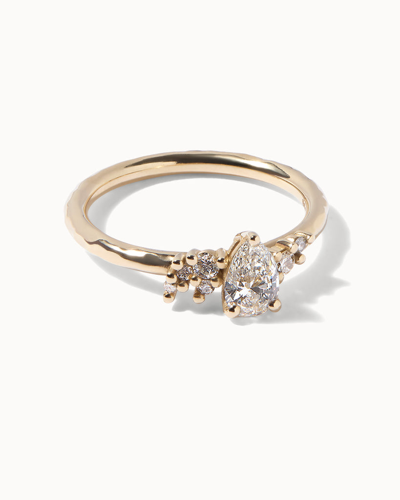 Solid gold engagement ring featuring a cluster of sparkling white diamonds surrounding a central 0.43ct pear cut diamond handcrafted in London by Maya Magal London