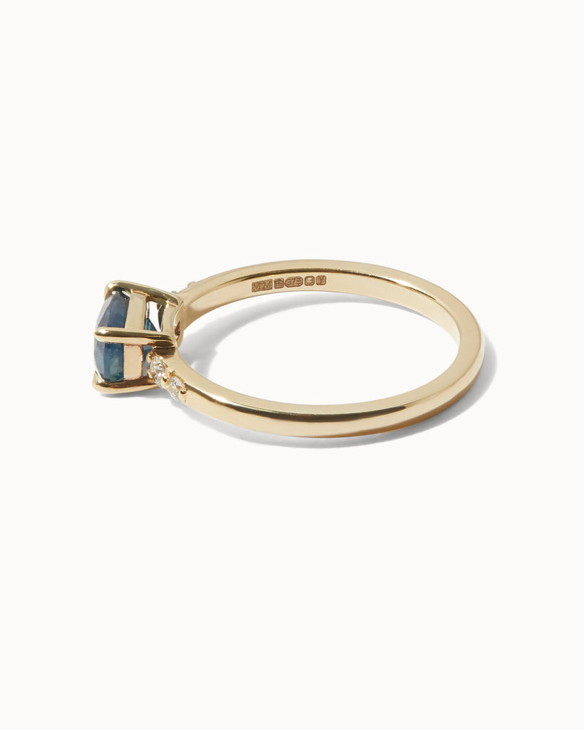 Solid gold engagement ring featuring an oval blue Sapphire and four round cut white diamonds on the sides handcrafted in London by Maya Magal London