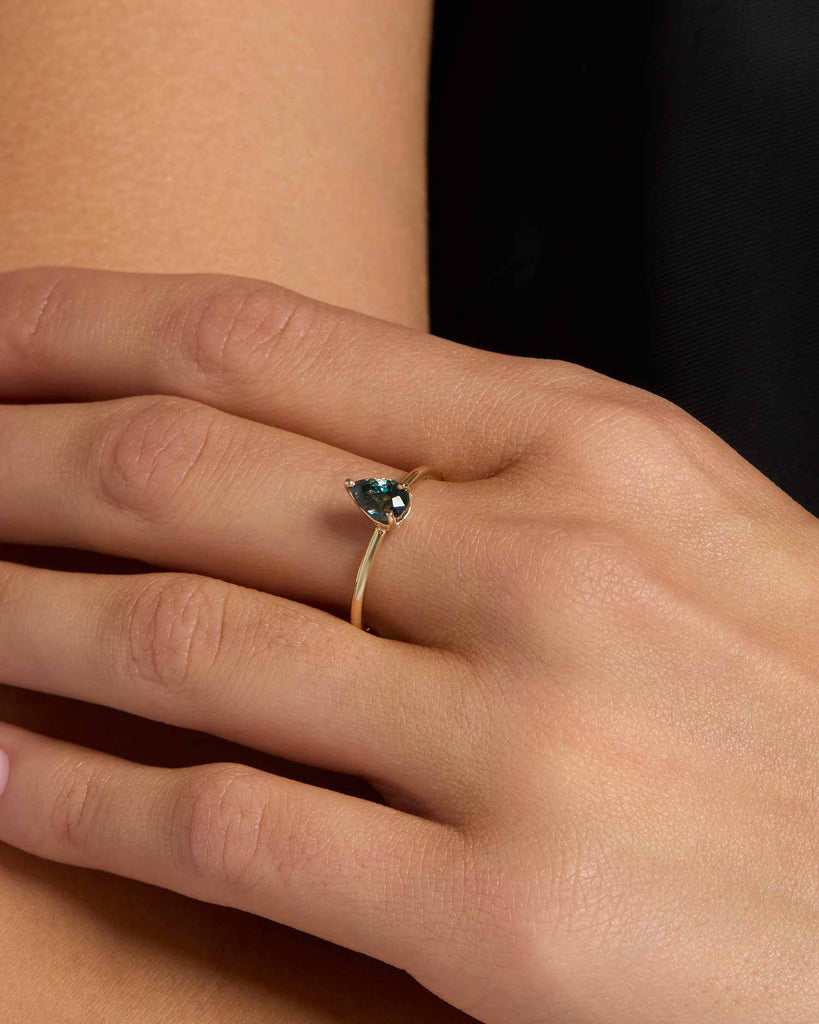 Solid gold solitaire engagement ring featuring a pear cut teal sapphire handcrafted in London by Maya Magal London