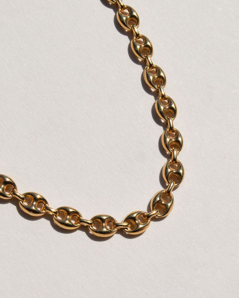 A close-up of a gold-toned chain necklace with elongated oval links, arranged on a light off-white background.