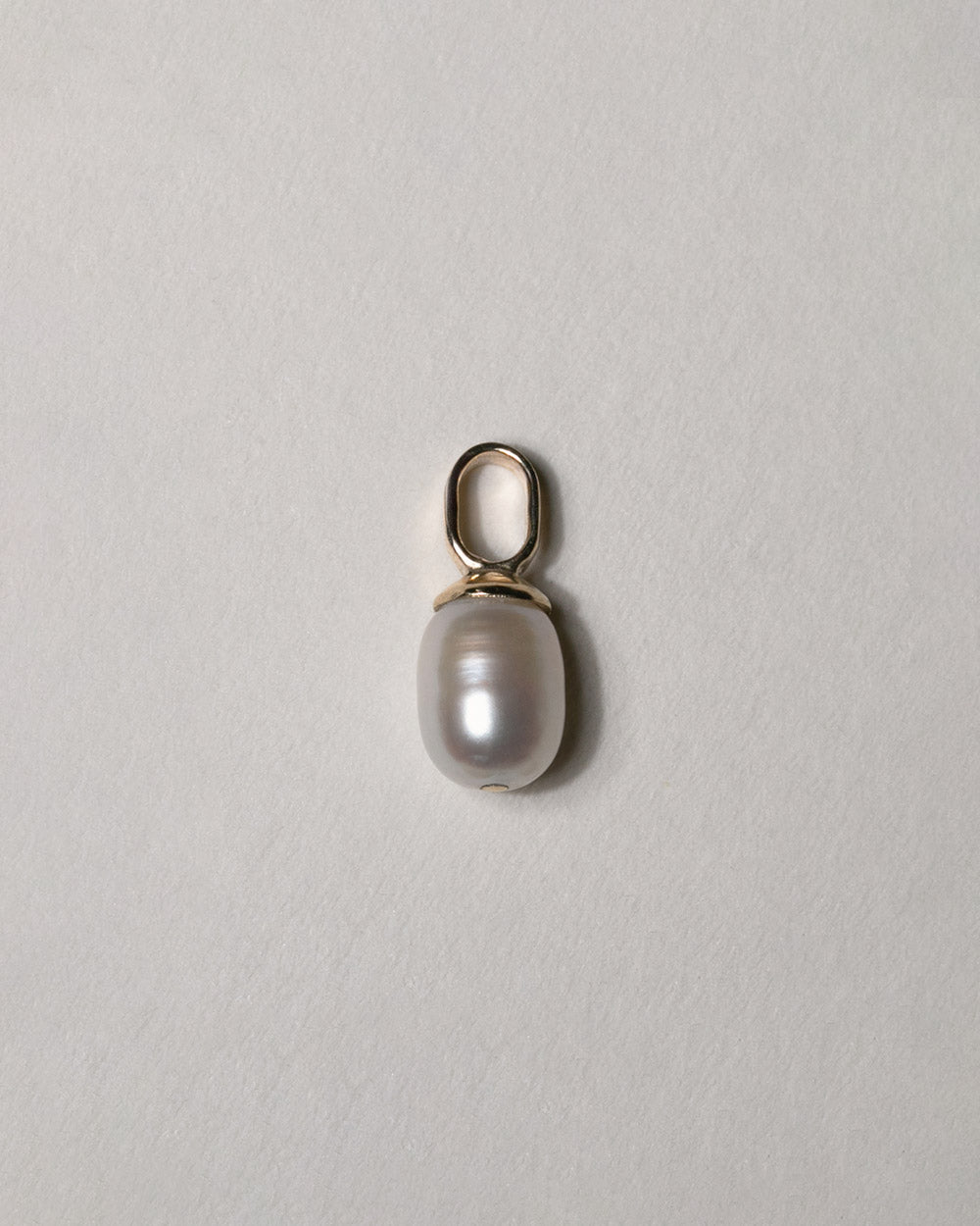 A pair of 9ct solid gold huggie hoop earrings with a dangling white baroque pearl, displayed on a textured beige background. Charm pictured by itself