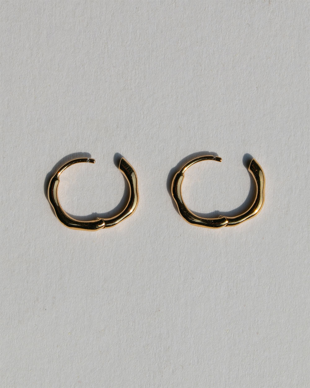 A pair of organic textured 18ct gold plated sterling silver hoop earrings. Side view. Made with recycled materials and sustainable practices. With open closure 