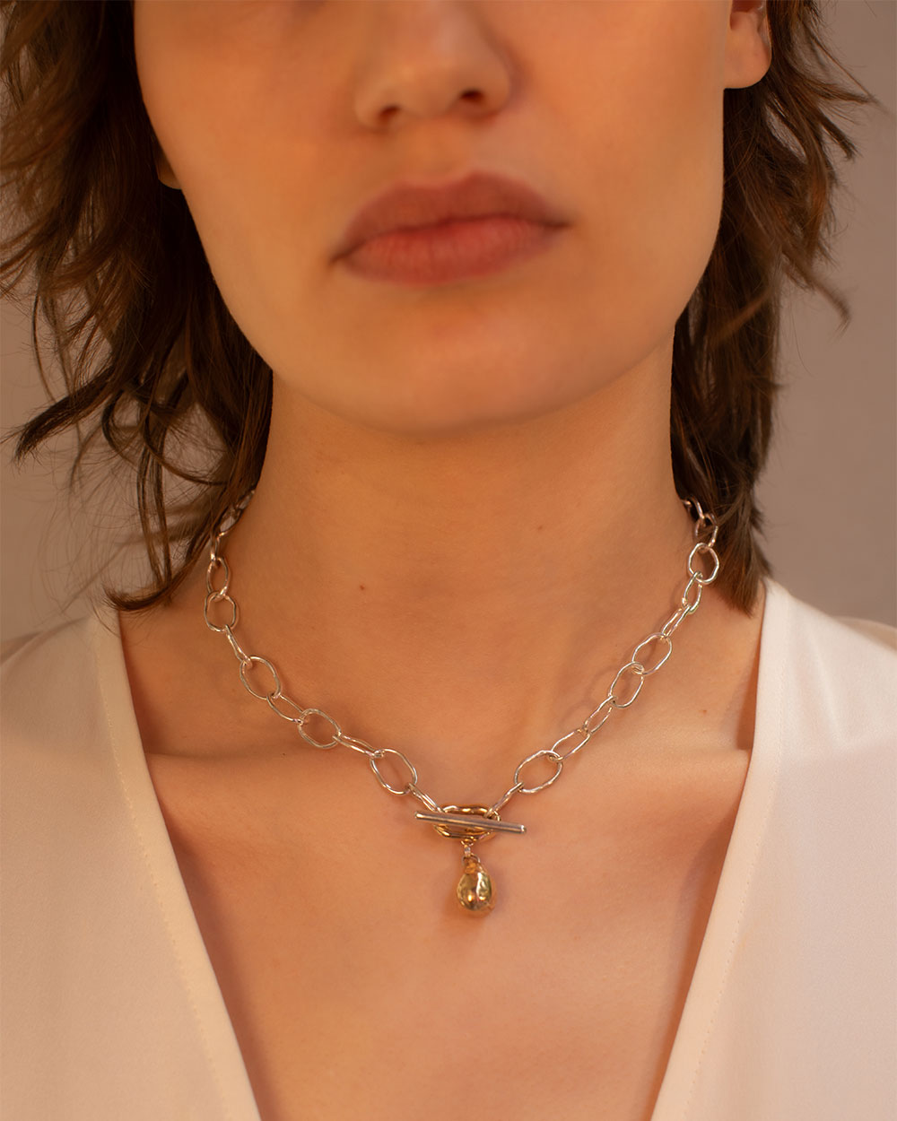 Close up of model wearing Sterling silver chain necklace with a 9ct gold drop charm and toggle clasp, photographed on a light textured background with natural shadows.