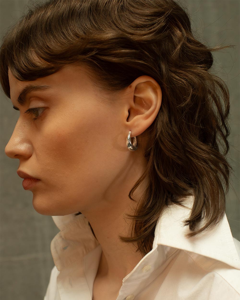 Side view of model wearing Sterling silver molten hoop earrings with a chunky organic texture.
