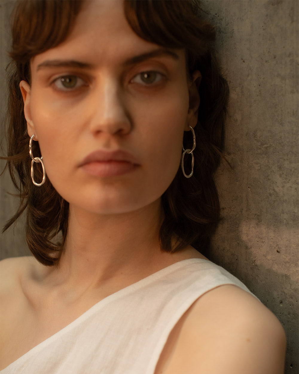 Front view of model wearing Sterling silver molten link hoop earrings with organic oval shapes, photographed on a light background with natural shadows.