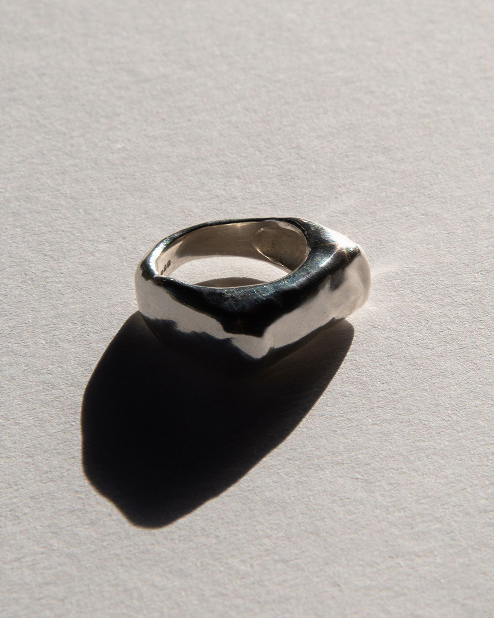 side view of Sterling silver Molten Light Ring with a chunky organic shape, photographed on a light textured background with natural shadows.