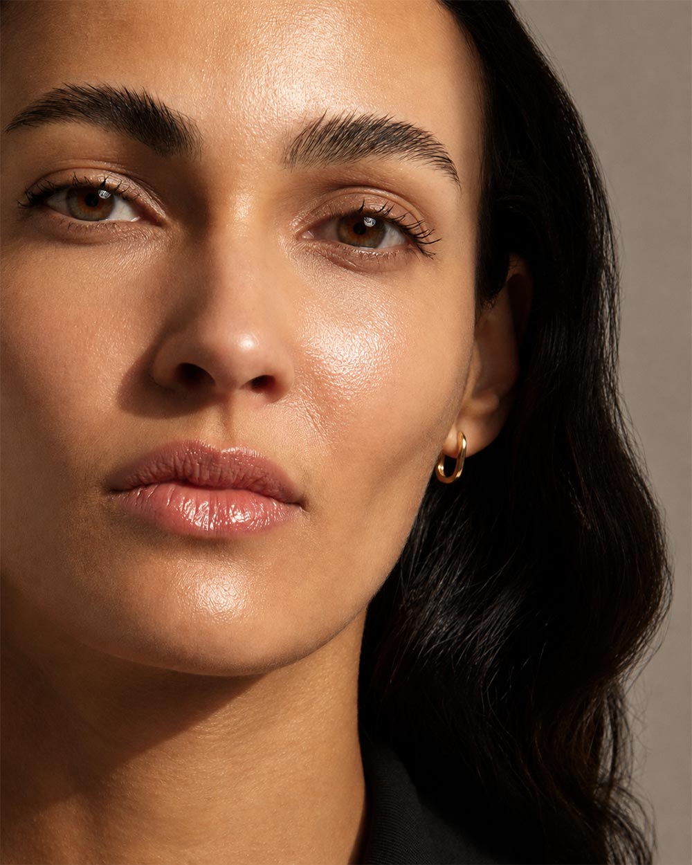 Front view of model wearing solid gold oval hoop earrings.