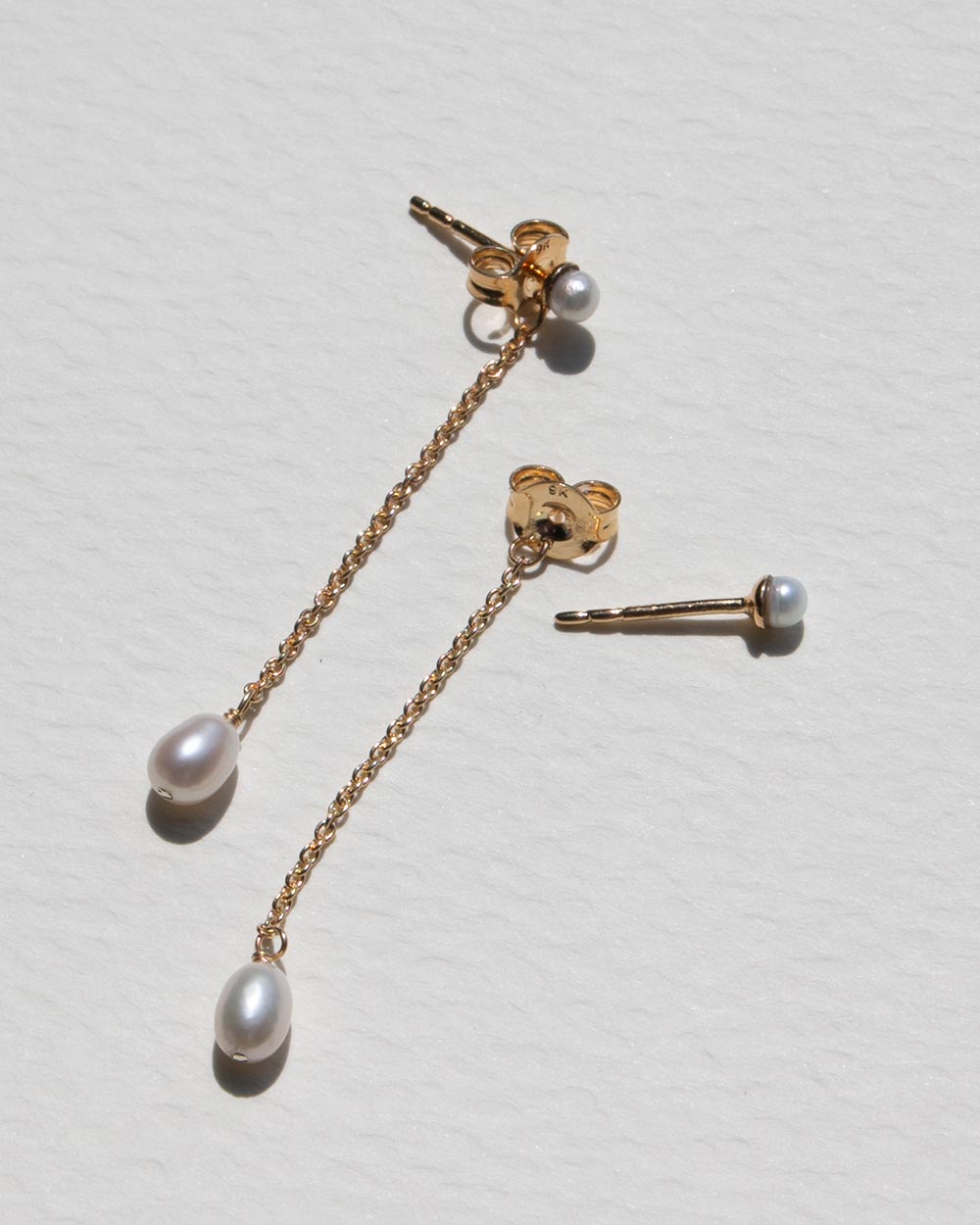 Side view of a pair of 9ct solid gold chain dangling earrings with a pearl pendant. Wtih closure undone. 