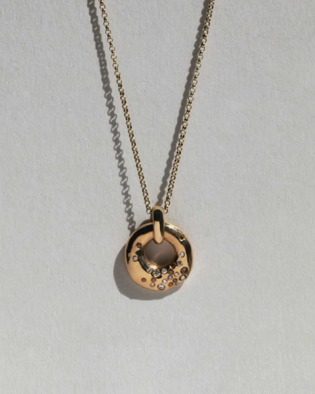 Video of 9 ct solid gold necklace with circular charm flush set with grey champage and white diamond.