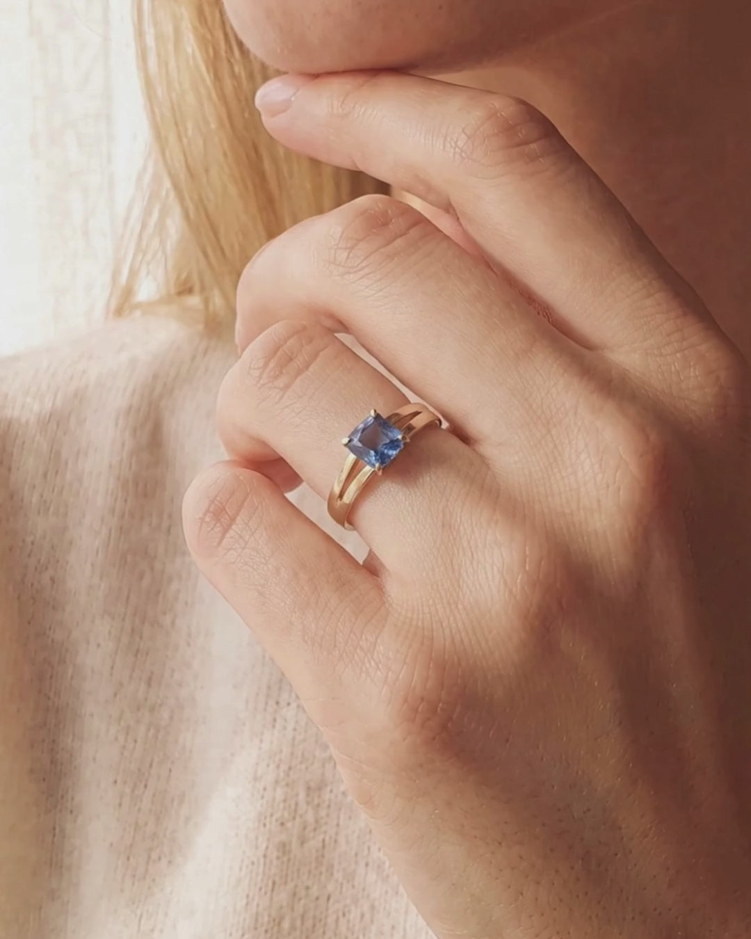 Video of model wearing 9ct solid recycled gold ring set with  1.11ct cushion-cut cornflower blue sapphire, selected for its luminous colour and natural beauty. Set in a classic four-claw solitaire, the gently sculpted split band draws the eye towards the centre stone, creating a balanced silhouette that feels both timeless and contemporary.