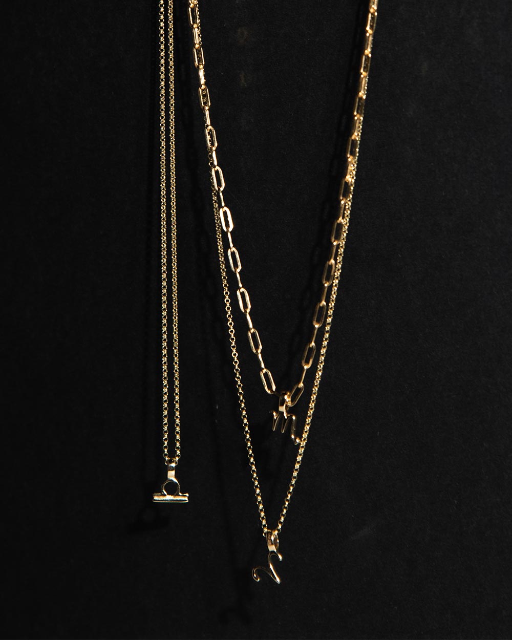 3 gold Zodiac Charms on chains displayed on black background 